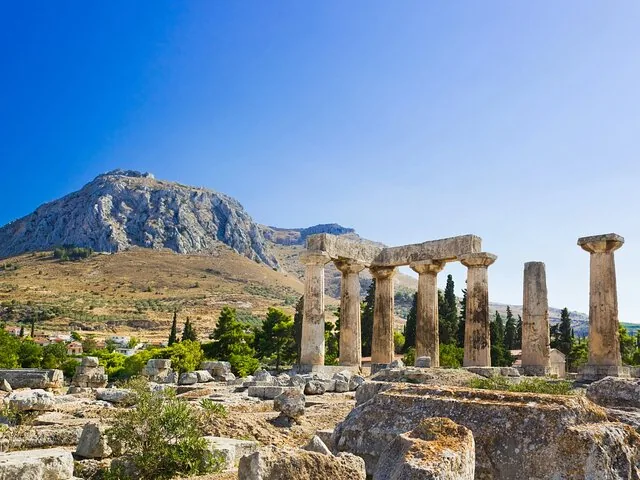 ancient ruins with tall columns and a mountain in the background under a blue sky