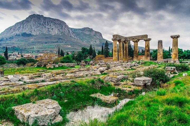 ancient ruins with columns and a large mountain in the background under a cloudy sky