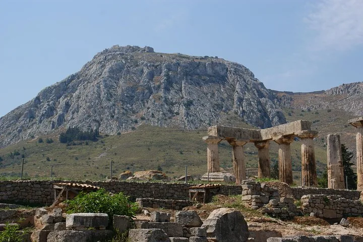 ancient ruins with columns and a large rocky mountain in the background