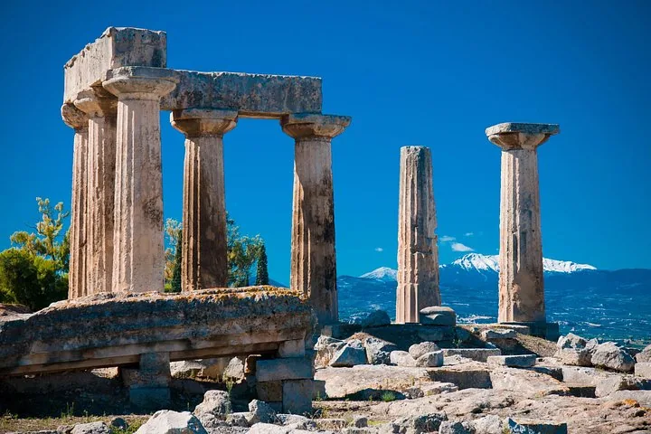 ancient ruins with tall columns and snow-capped mountains in the background under a blue sky